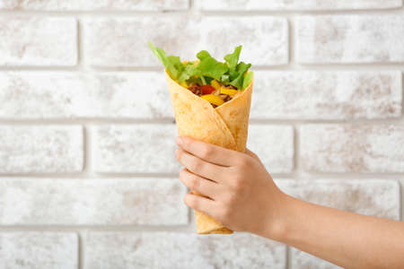 Female hand with tasty doner kebab on brick backgroundの写真素材