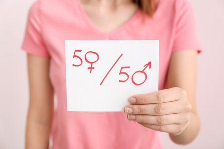 Woman holding paper sheet with simple fraction and symbols of woman and man on color background, closeup. Concept of feminismの写真素材