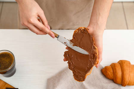 Woman spreading chocolate onto fresh croissant in kitchenの写真素材