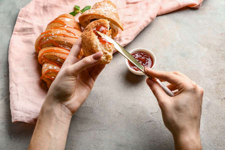 Woman spreading jam onto fresh croissant at tableの写真素材