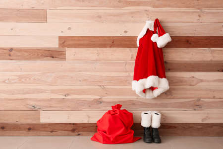 Santa Claus costume hanging on wooden wall near shoes and bag in roomの写真素材