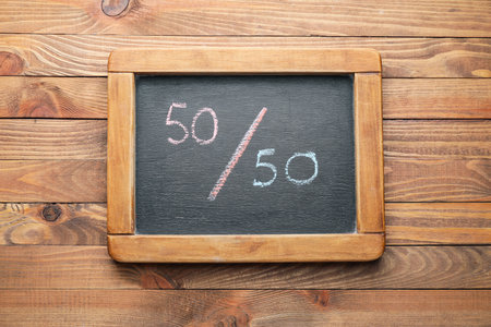 Chalkboard with written simple fraction on wooden background. Concept of feminismの写真素材