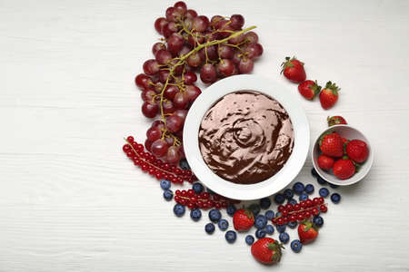 Bowl with tasty chocolate fondue and berries on white tableの写真素材