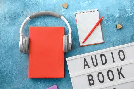 Book and modern headphones on color background. Concept of audiobookの写真素材