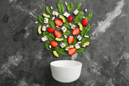 Bowl and ingredients for tasty salad on gray background