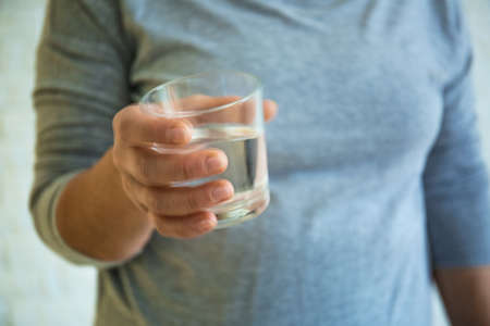 Senior woman with glass of water suffering from Parkinson syndrome, closeup