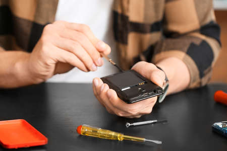 Electronic technician repairing mobile phone in service center, closeup