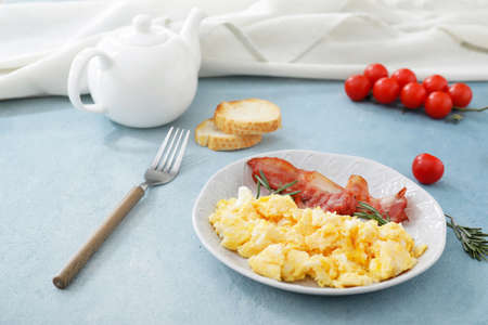 Plate with scrambled egg and bacon on color background
