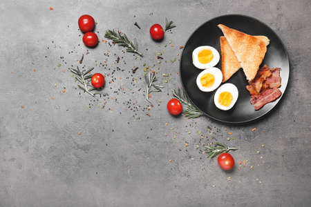 Plate with boiled eggs, bacon and toasted bread on dark background