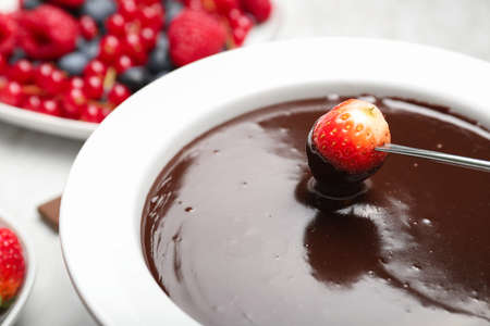 Dipping of tasty strawberry into bowl with chocolate fondue on table, closeupの写真素材