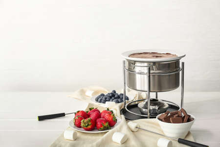 Fondue pot with melted chocolate and berries on tableの写真素材