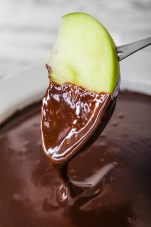 Dipping of tasty apple into bowl with chocolate fondue, closeupの写真素材