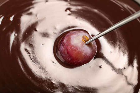 Dipping of tasty grape into chocolate fondue, closeupの写真素材