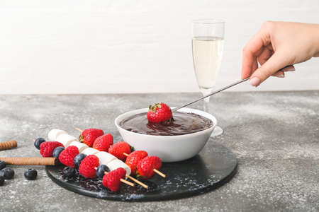 Woman dipping tasty strawberry into bowl with chocolate fondue on tableの写真素材