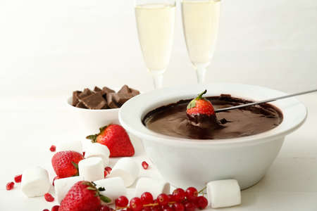 Dipping of tasty strawberry into bowl with chocolate fondue on tableの写真素材