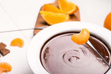 Dipping of tasty tangerine into bowl with chocolate fondue on table, closeupの写真素材