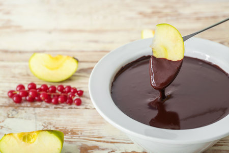 Dipping of tasty apple into bowl with chocolate fondue on tableの写真素材