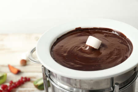 Dipping of tasty marshmallow into bowl with chocolate fondue on table, closeupの写真素材