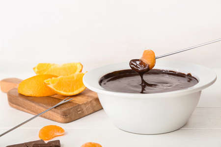 Dipping of tasty tangerine into bowl with chocolate fondue on tableの写真素材
