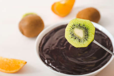 Dipping of tasty kiwi into bowl with chocolate fondue on table, closeupの写真素材