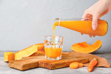 Woman pouring vegetable juice into glass on table