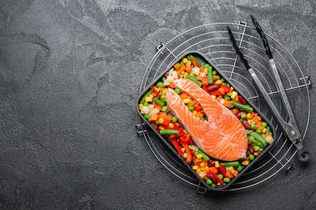 Baking dish with raw salmon steak and vegetables on dark backgroundの写真素材