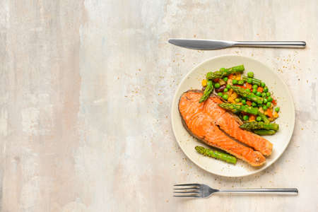 Plate with fried salmon and vegetables on tableの写真素材