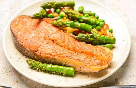 Plate with fried salmon and vegetables on tableの写真素材