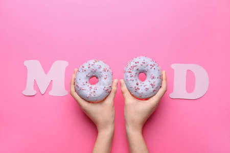 Female hands with tasty donuts and word MOOD on color backgroundの写真素材