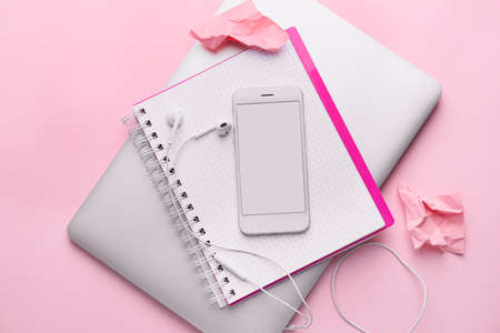 Mobile phone with notebook and laptop on pink background