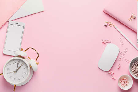 Mobile phone with computer mouse, stationery and alarm clock on pink background
