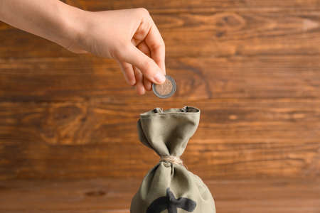 Female hand putting coin into bag with money on wooden backgroundの写真素材