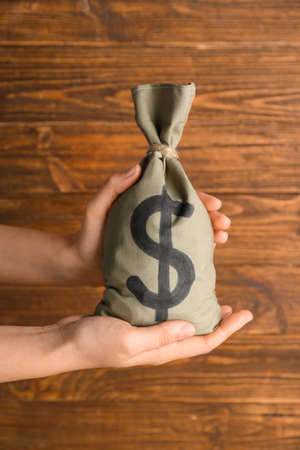 Female hands holding bag with money on wooden backgroundの写真素材