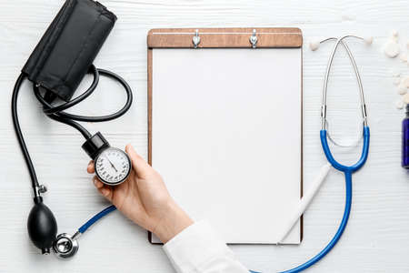 Hand of doctor with sphygmomanometer, clipboard and pills on white backgroundの写真素材