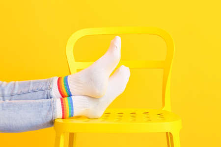 Legs of young woman in socks on chair against color backgroundの写真素材