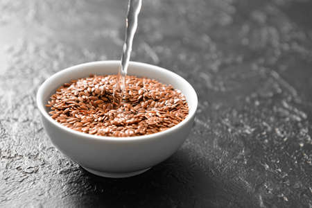 Pouring of water in bowl with flax seeds on dark backgroundの写真素材