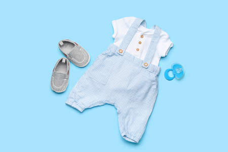 Baby clothes with booties and pacifier on color background