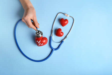 Female hand with red hearts and stethoscope on color background. Cardiology conceptの写真素材