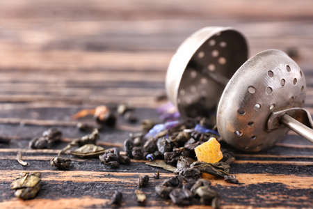 Strainer with dry tea leaves on wooden table