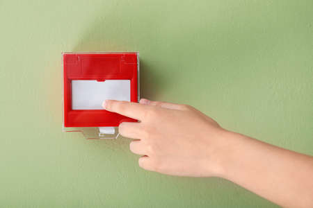 Hand of person near manual call point mounted on wall