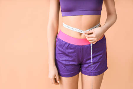Young woman with measuring tape on color background. Weight loss conceptの写真素材