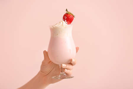 Female hand with glass of tasty milkshake on color backgroundの写真素材