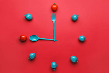 Creative clock made of tomatoes and cutlery on color backgroundの写真素材