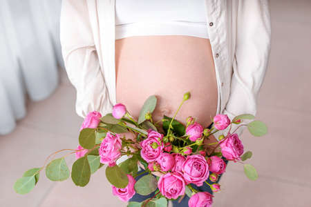 Beautiful pregnant woman with bouquet of flowers at home, closeupの写真素材