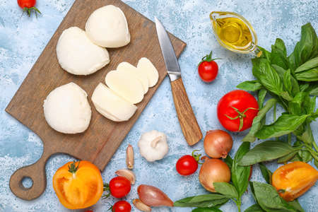 Cutting board with mozzarella cheese, oil and vegetables on color backgroundの写真素材