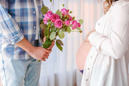 Husband giving bouquet of flowers to his pregnant wife at homeの写真素材