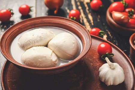 Mozzarella cheese in bowl on dark wooden background