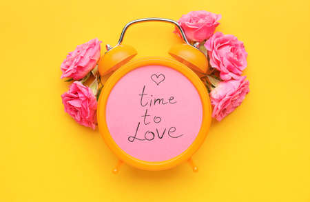 Alarm clock with flowers and text TIME TO LOVE on color backgroundの写真素材