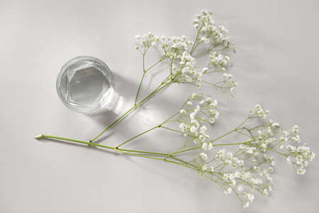 Glass of clean water and flowers on light backgroundの写真素材