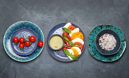Mozzarella cheese with tomatoes, basil, spices and oil on dark background